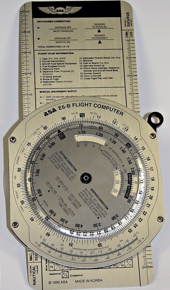 Calculateur de navigation en métal : une règle rectangulaire portant un disque tournant gradué de plusieurs échelles circulaires, avec des inscriptions techniques.