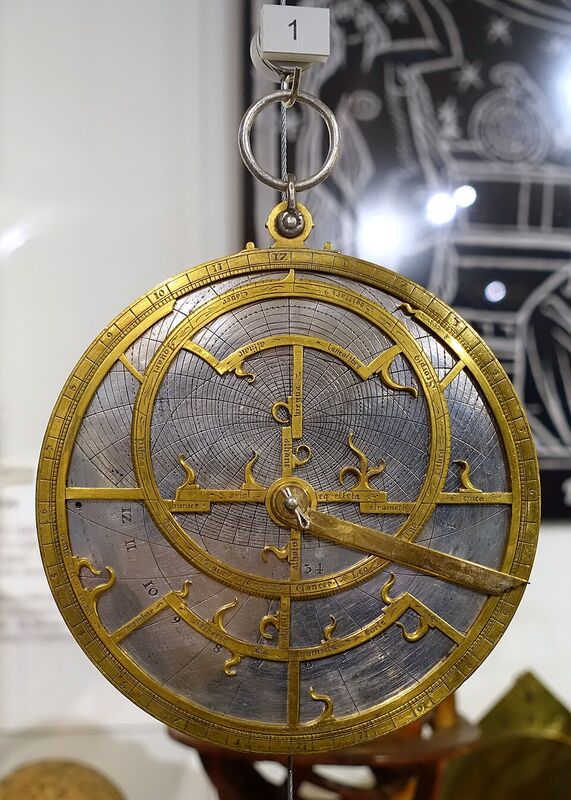 Astrolabe en laiton doré suspendu à un anneau : un disque gradué sur son bord, recouvert d'une plaque ajourée en forme de feuillages dont les pointes indiquent des étoiles.