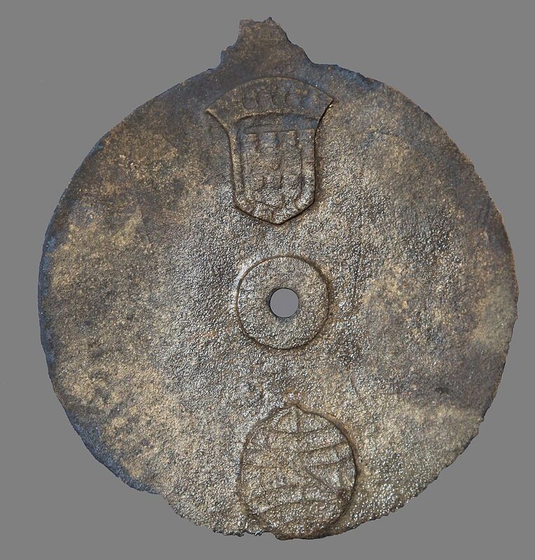 Disque de bronze corrodé, percé d'un trou au centre, portant en relief des armoiries en haut et une sphère armillaire en bas.