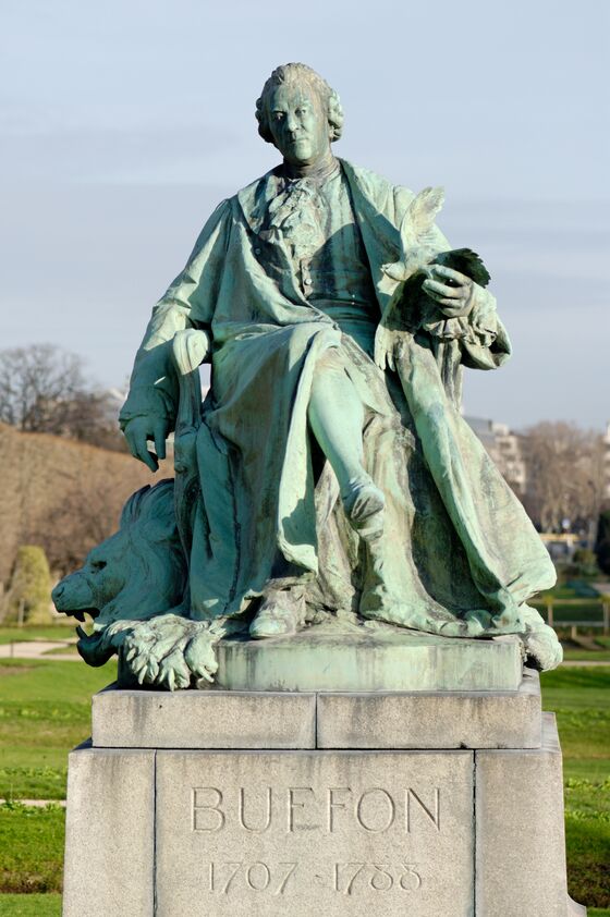 Statue de bronze verdi d'un homme assis dans un fauteuil, une plume à la main, posée sur un socle de pierre portant l'inscription BUFFON 1707-1788, dans un jardin.