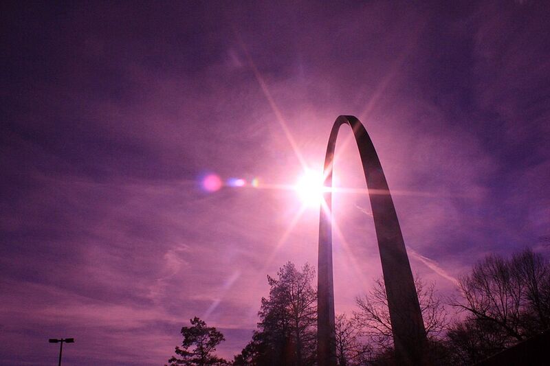 Photographie d'un immense arc en acier inoxydable, brillant au soleil, sur un ciel bleu.