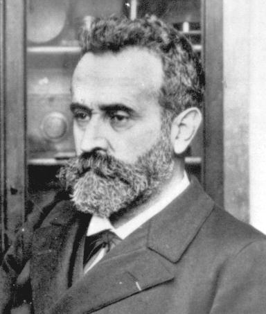 Photographie en noir et blanc : un homme d'une quarantaine d'années, barbe grisonnante, de trois quarts, devant une vitrine.
