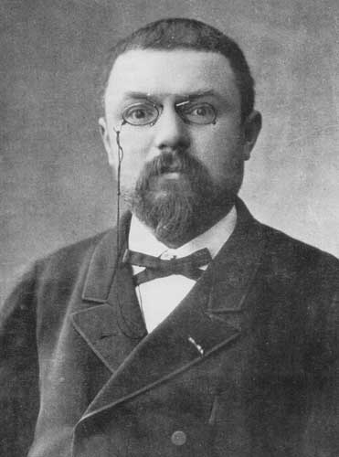 Photographie en noir et blanc : portrait d'un homme barbu à lunettes, en costume sombre.