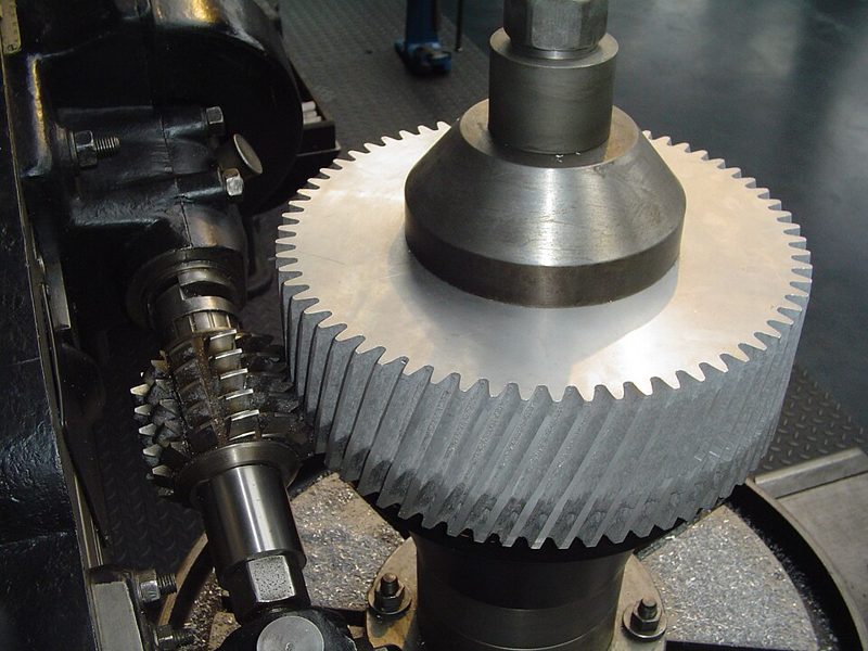 Une fraise-mère, à gauche, taille les dents d'une grande roue dentée métallique sur une machine.