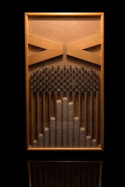 Une planche de Galton en bois et verre : des billes se sont accumulées en colonnes formant une cloche.