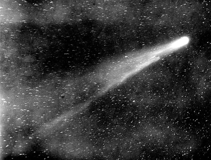 Photographie astronomique en noir et blanc : une comète à longue queue lumineuse sur un fond d'étoiles.