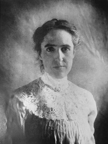 Photographie ancienne en noir et blanc : portrait d'une jeune femme aux cheveux relevés, en chemisier clair, regardant vers la droite.
