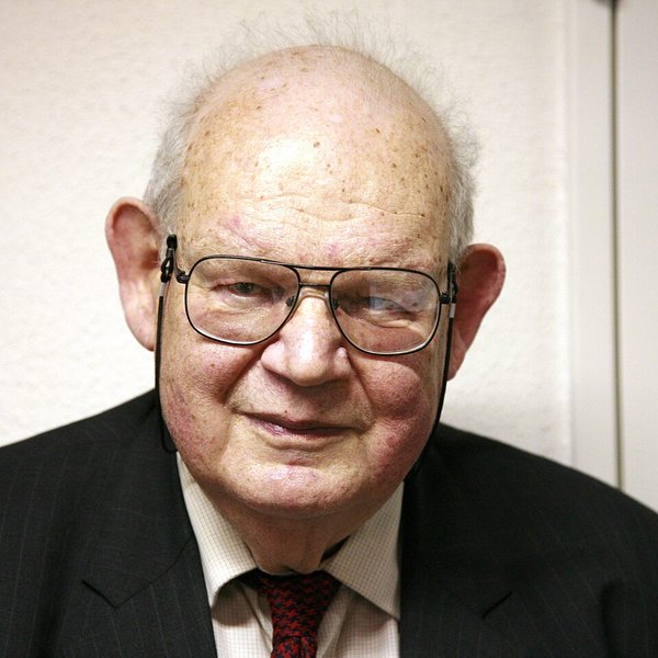 Photographie en couleurs de Benoît Mandelbrot âgé, souriant, devant un fond sombre.