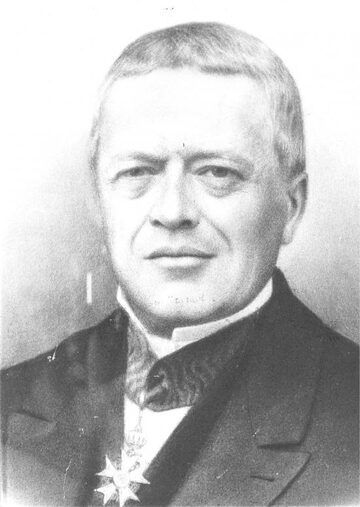 Portrait photographique ancien en noir et blanc d'un homme aux cheveux gris, en habit sombre, portant une décoration.