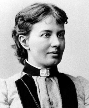 Photographie ancienne en noir et blanc d'une femme aux cheveux courts et bouclés, en col blanc, de face.