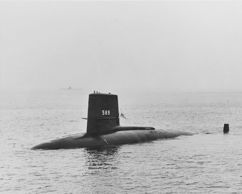 Photographie en noir et blanc : un sous-marin à coque noire, portant le numéro 589 sur son kiosque, navigue en surface sur une mer calme.
