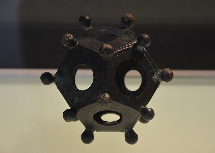Un petit dodécaèdre romain en bronze, ajouré, avec une boule à chaque sommet, dans une vitrine de musée.
