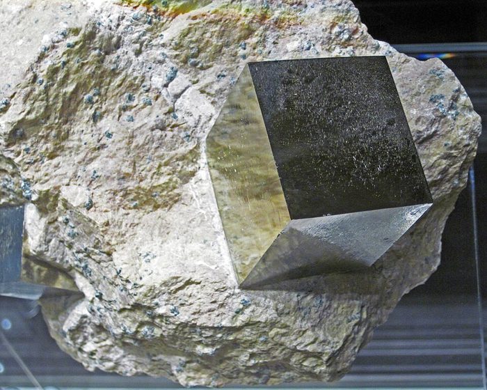 Un cristal de pyrite parfaitement cubique, doré, pris dans une roche claire.
