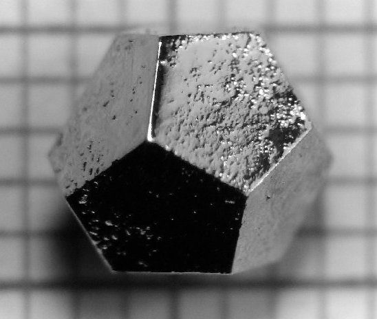 Un petit quasicristal métallique en forme de dodécaèdre régulier, posé sur du papier millimétré.