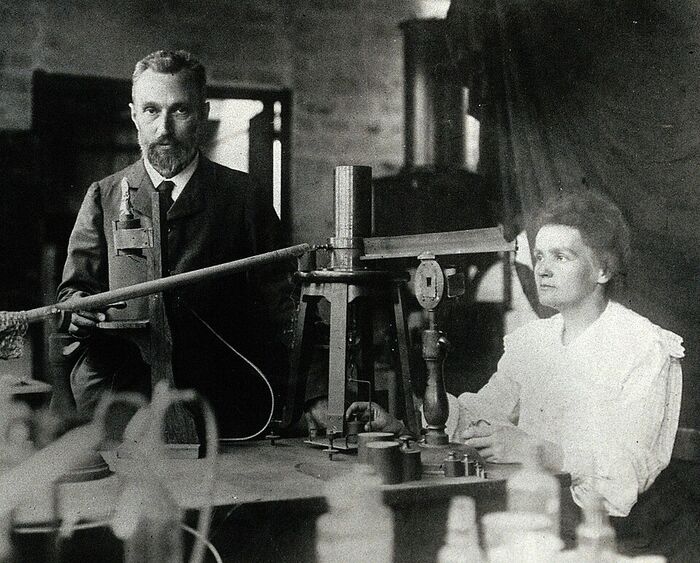 Photographie ancienne en noir et blanc : un homme et une femme debout dans un laboratoire, à côté d'un appareil de mesure posé sur une table.