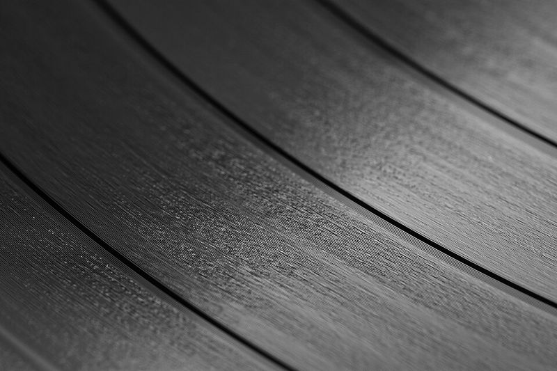 Gros plan en noir et blanc sur la surface d'un disque vinyle : des bandes de sillons très fins, séparées par des lignes plus sombres entre les morceaux.