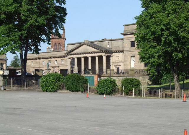 Façade d'un bâtiment néoclassique en pierre claire, avec une colonnade, sur une place.