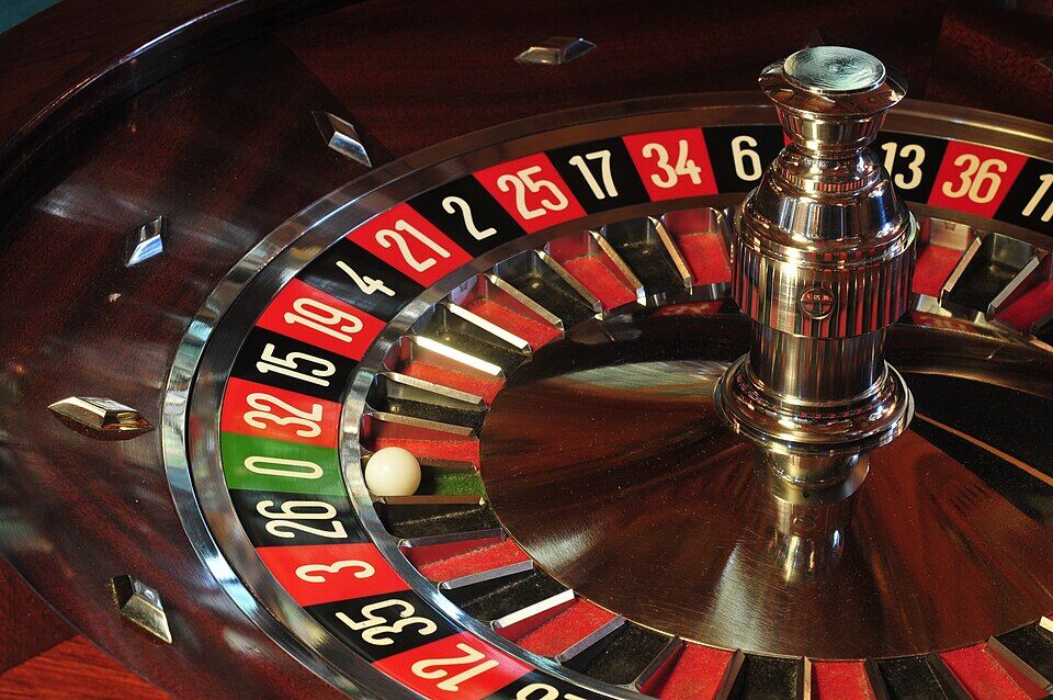 Gros plan sur un cylindre de roulette en bois verni, avec ses cases rouges, noires et le zéro vert ; une bille blanche est arrêtée dans une case.