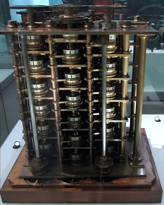 Un mécanisme en laiton dans une vitrine : des colonnes de roues dentées portant des chiffres, empilées entre deux plaques et actionnées par une manivelle.
