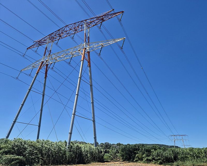 Pylône métallique en treillis d'une ligne à très haute tension, avec plusieurs câbles suspendus à des isolateurs, sur fond de ciel.